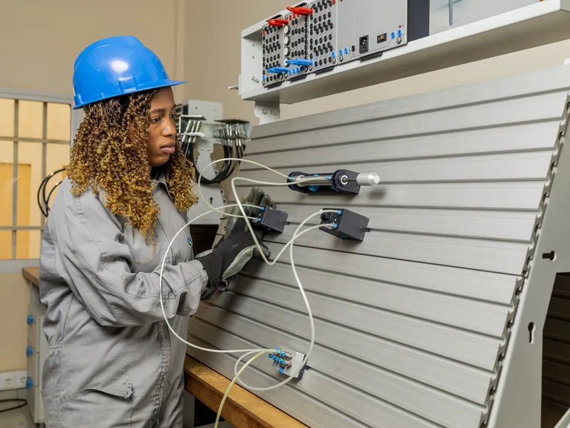 Aluna de capacete azul a ligar cabos num painel de montagem eléctrica