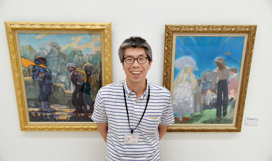 安田朗さんのイラスト原画を前に笑顔をみせる兵庫県立美術館の小林公