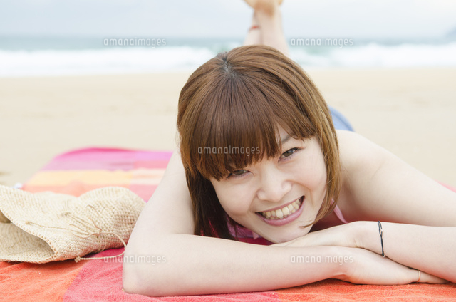 ビーチに寝そべって笑うビキニ姿の女性[10568001053]の写真・イラスト